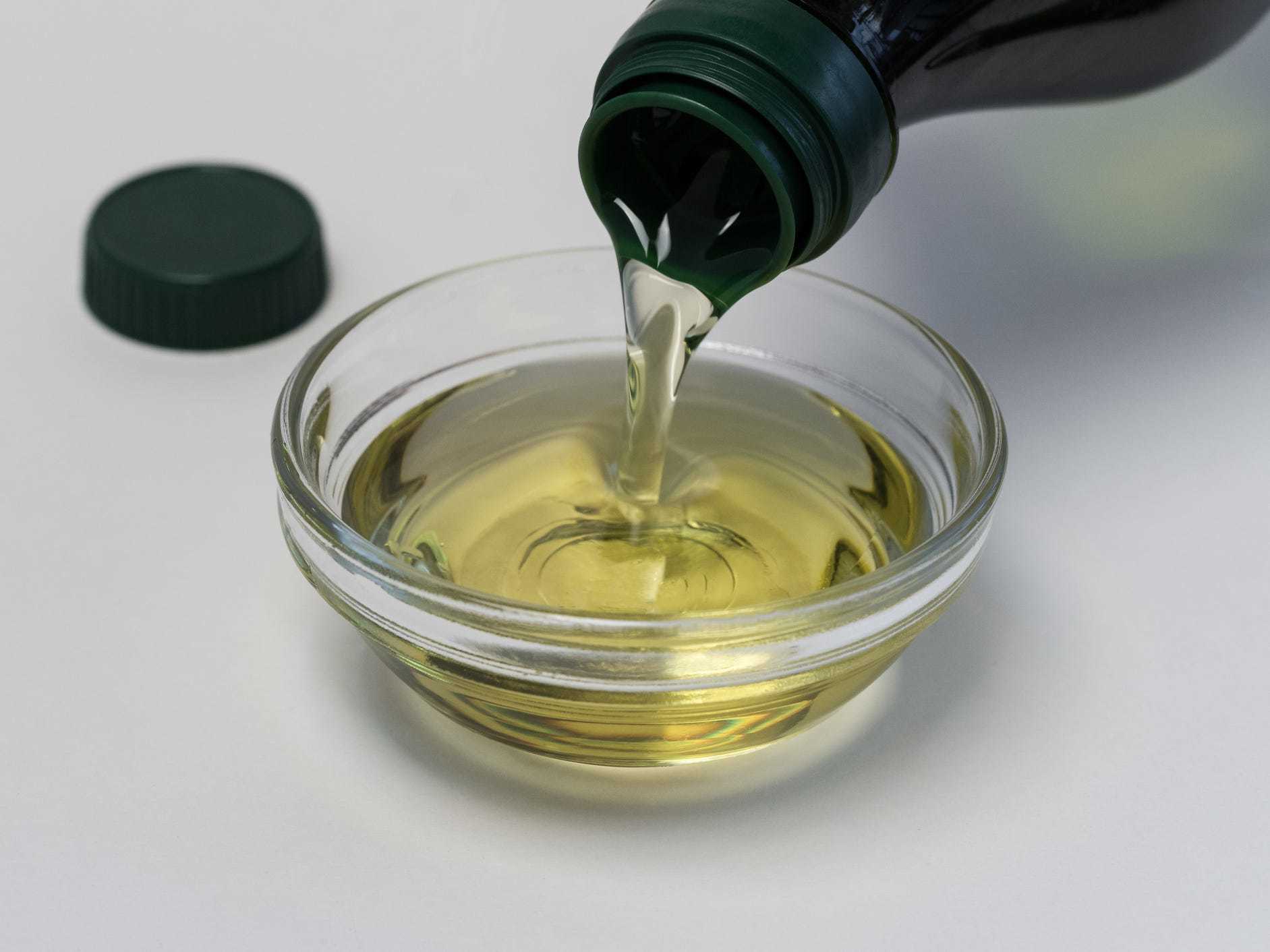 Grapeseed oil is poured into a small glass bowl atop of a white background.