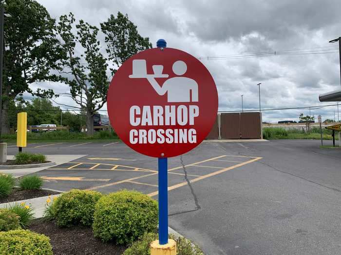 Carhops bring out food and drinks to customers waiting in parking spots.