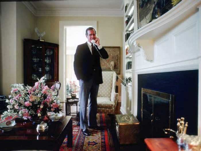 Bush took a call in a sitting room furnished with beige walls, a rich colored rug, and a neutral patterned chair.