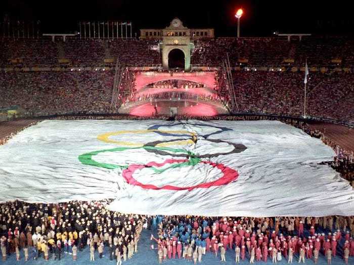 THEN: Barcelona 1992 - A giant Olympic flag covers the pitch during the opening ceremony of the XXVth summer Olympic Games at Montjuic stadium.