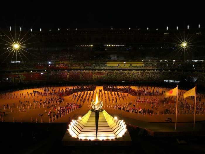 NOW: Tokyo 2020 - Athletes and other opening ceremony participants social distance as the Olympic torch is lit.