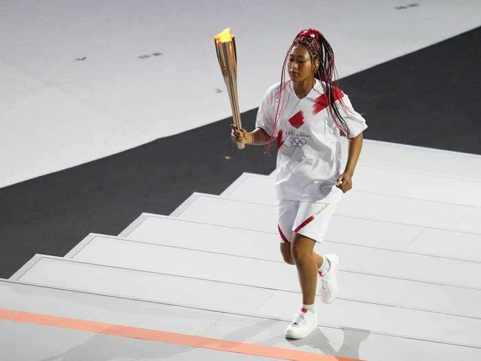 NOW: Tokyo 2020 - Tennis star Naomi Osaka carries the Olympic torch during the Tokyo 2020 Olympic Games opening ceremony at a fan-less Olympic Stadium.