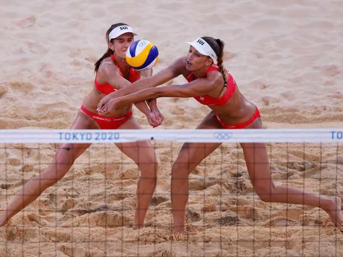 7/24: Anouk Verge-Depre and Joana Heidrich of Team Switzerland cross arms during beach volleyball at the Tokyo 2020 Olympics.