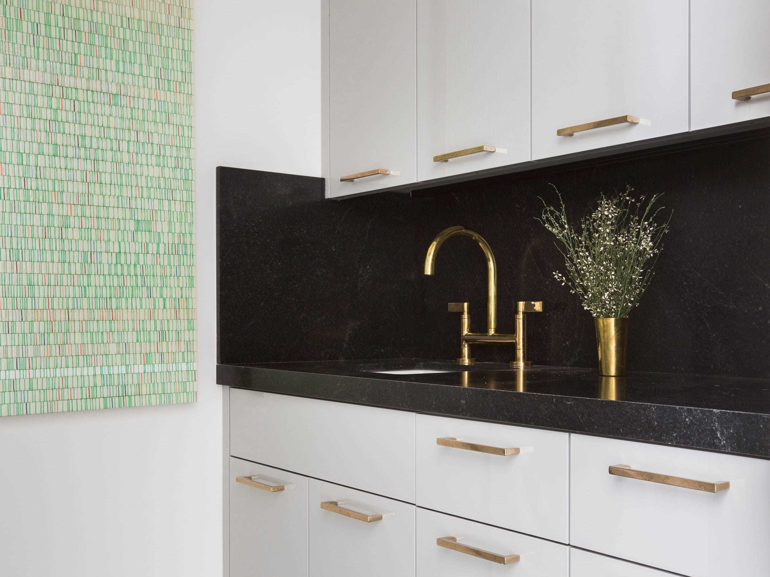 A shot of a gold sink with black tile and white cabinets.