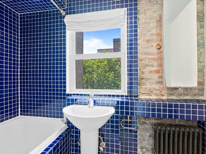 The only bathroom in the home contrasts a blue, tile backsplash with exposed brick.