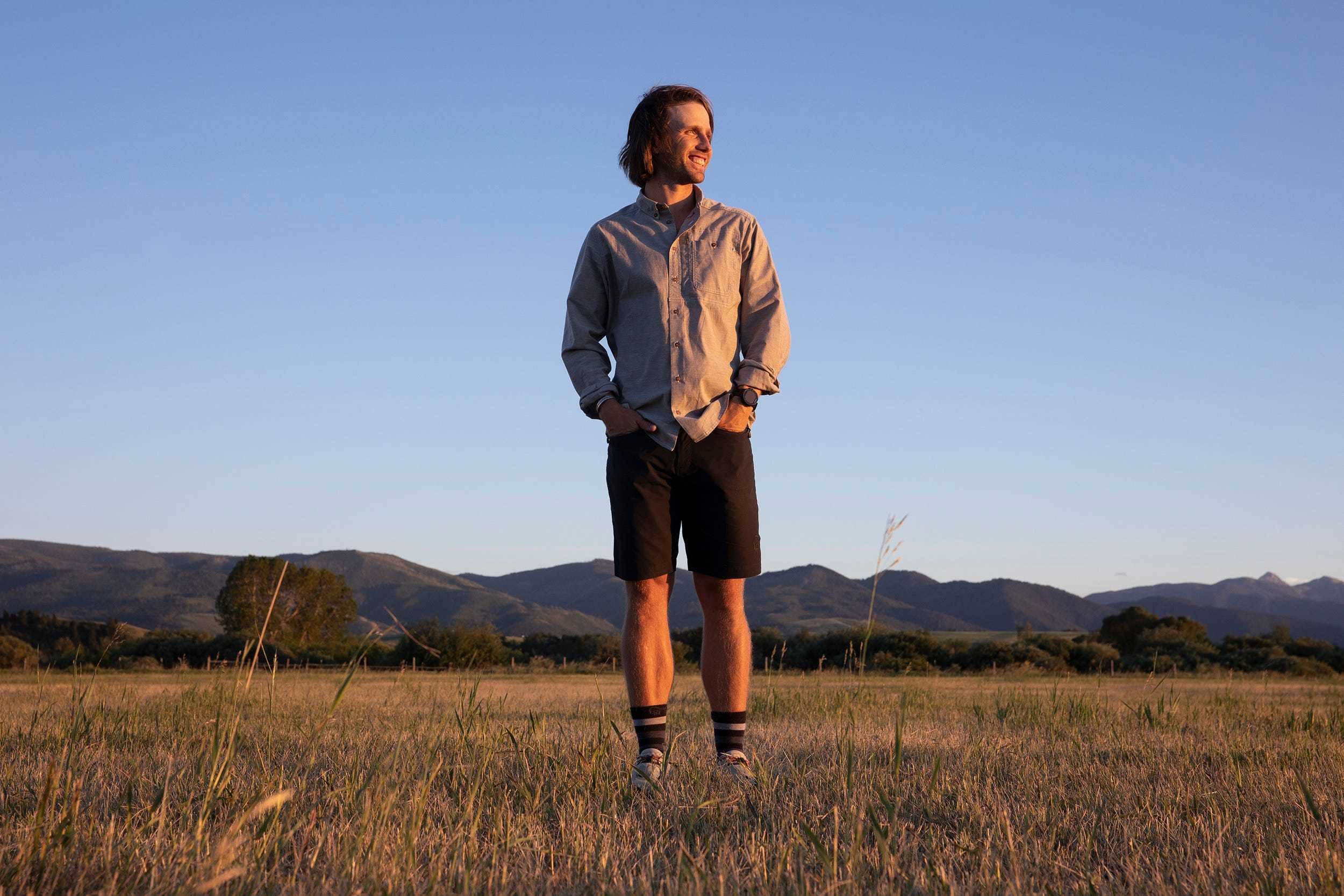 Ecologist Charles Post wears a gray button-up shirt with black shorts and striped long socks while posing in an open field.