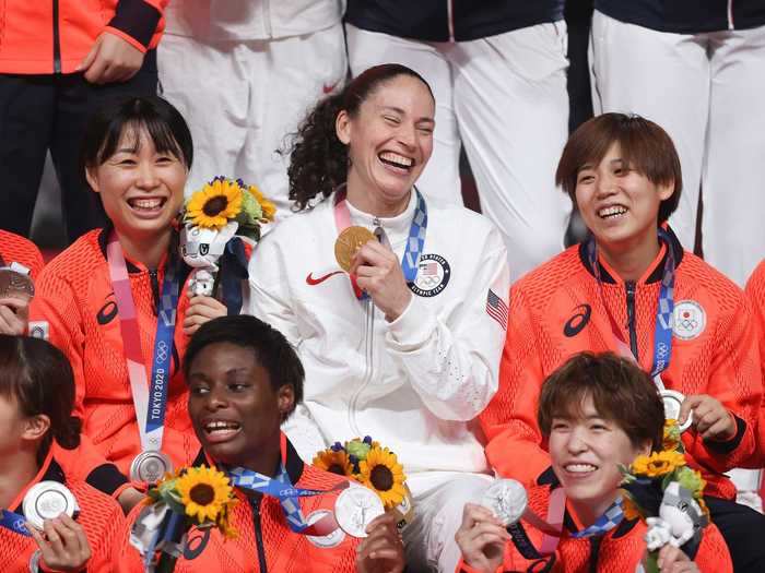 Sue Bird grins with her gold medal while surrounded by silver medalists from Team Japan.