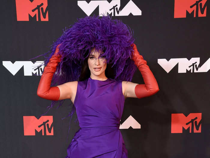 Kacey Musgraves stepped onto the red carpet in an eye-catching purple dress and feather-filled hat from the Valentino fall 2021 collection.