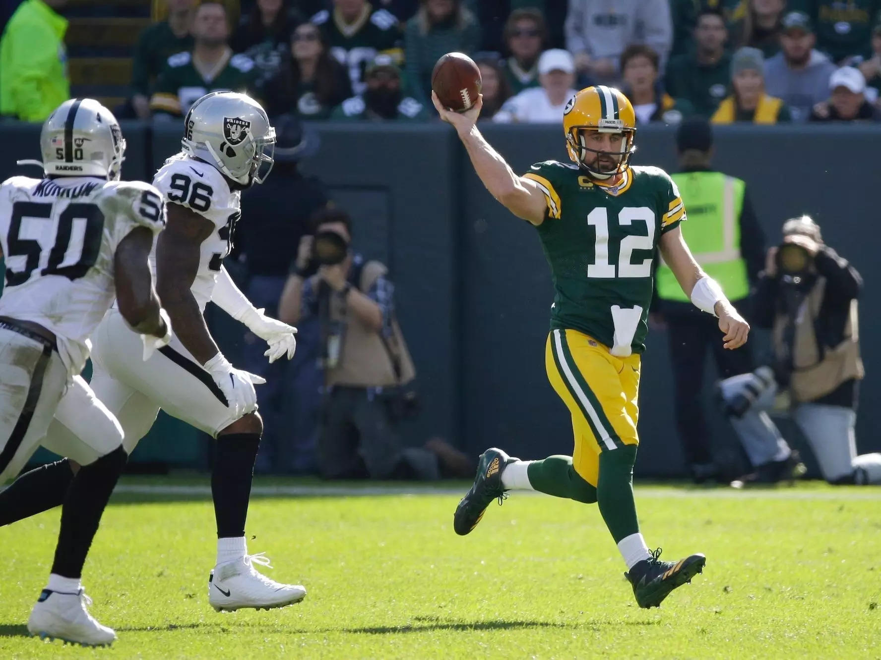 Aaron Rodgers makes a throw off the wrong foot while being chased by Raiders defenders.