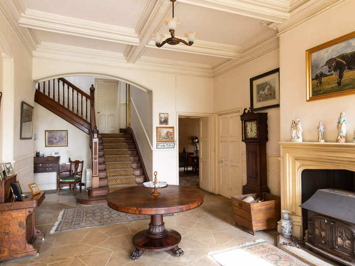 Views of the main house hallway showcase the features that make a traditional English manor house - a wooden grandfather clock, wrap-around staircases, and fireplaces.