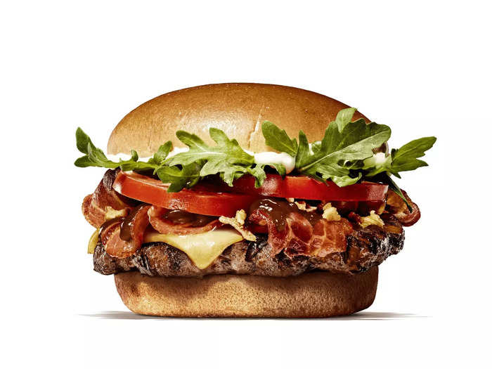 The new Steakhouse burger is topped with bacon, oak smoked cheddar cheese, tomatoes, onions, arugula, mayo, and BBQ sauce, all in a brioche bun.