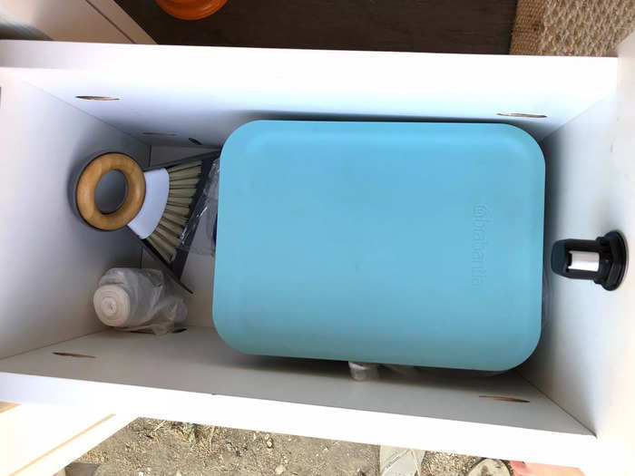 A drawer with a small garbage can pulled out from the side of the sink.