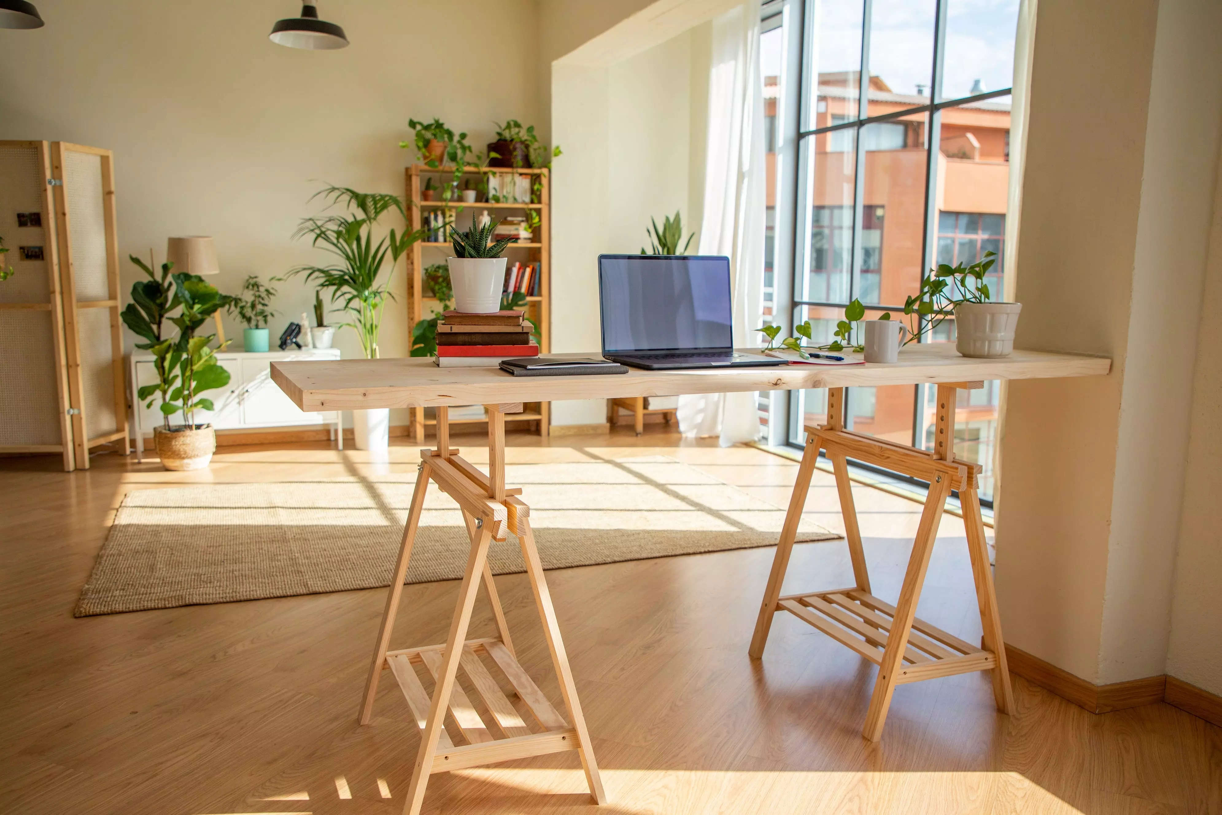 An open room with plants, tall windows, and a laptop resting on a Nordic desk