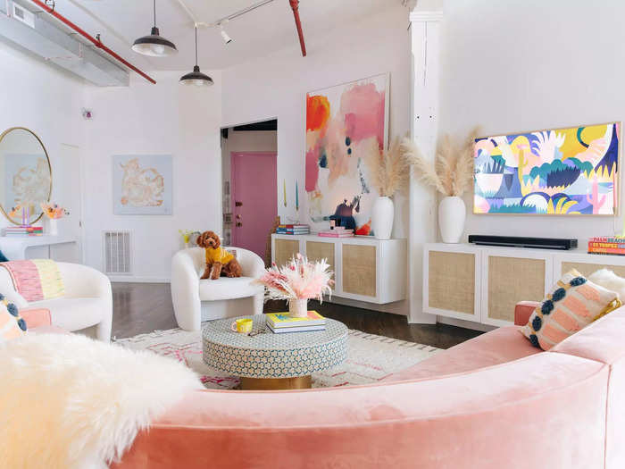 The apartment has distinct pastel interiors, exposed brick walls, a pink floor-to-ceiling shelving unit, and an at-home bar.