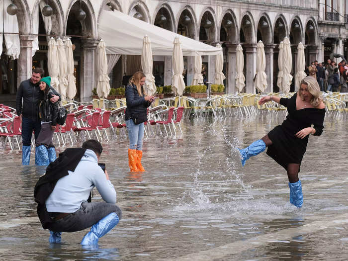 Tourists wear makeshift rain boots to wade through the flooded cafes and squares - others prefer to go barefoot.