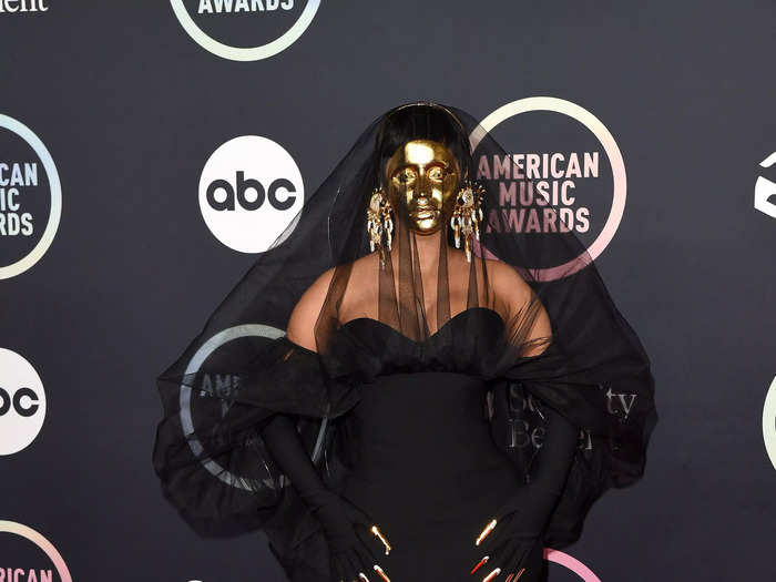 Cardi B arrived on the red carpet wearing a custom Schiaparelli gown. She accessorized with a gold mask and bedazzled gold finger earrings.