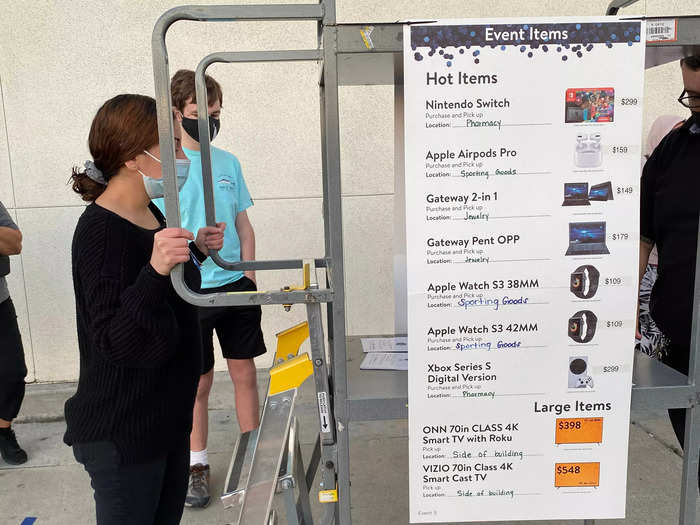 As customers waited in line, two employees wheeled a cart around adorned with a large poster that featured the "Hot Items" that were on sale for the holiday. Included were: Nintendo Switch, Apple Airpods Pro, Gateway computers, various Apple Watches, an Xbox Series S, and two SmartCast TVs.