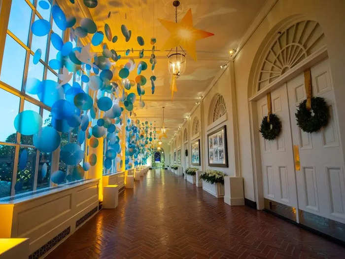In the East Colonnade, glowing stars and dove cutouts hang amid blue window decorations.