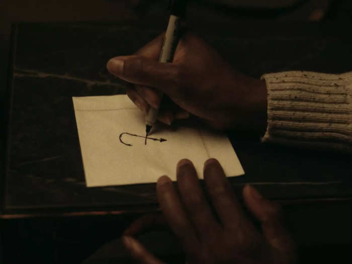 Miranda doodles the J-shaped cross symbol on a napkin after she and Arthur first meet.