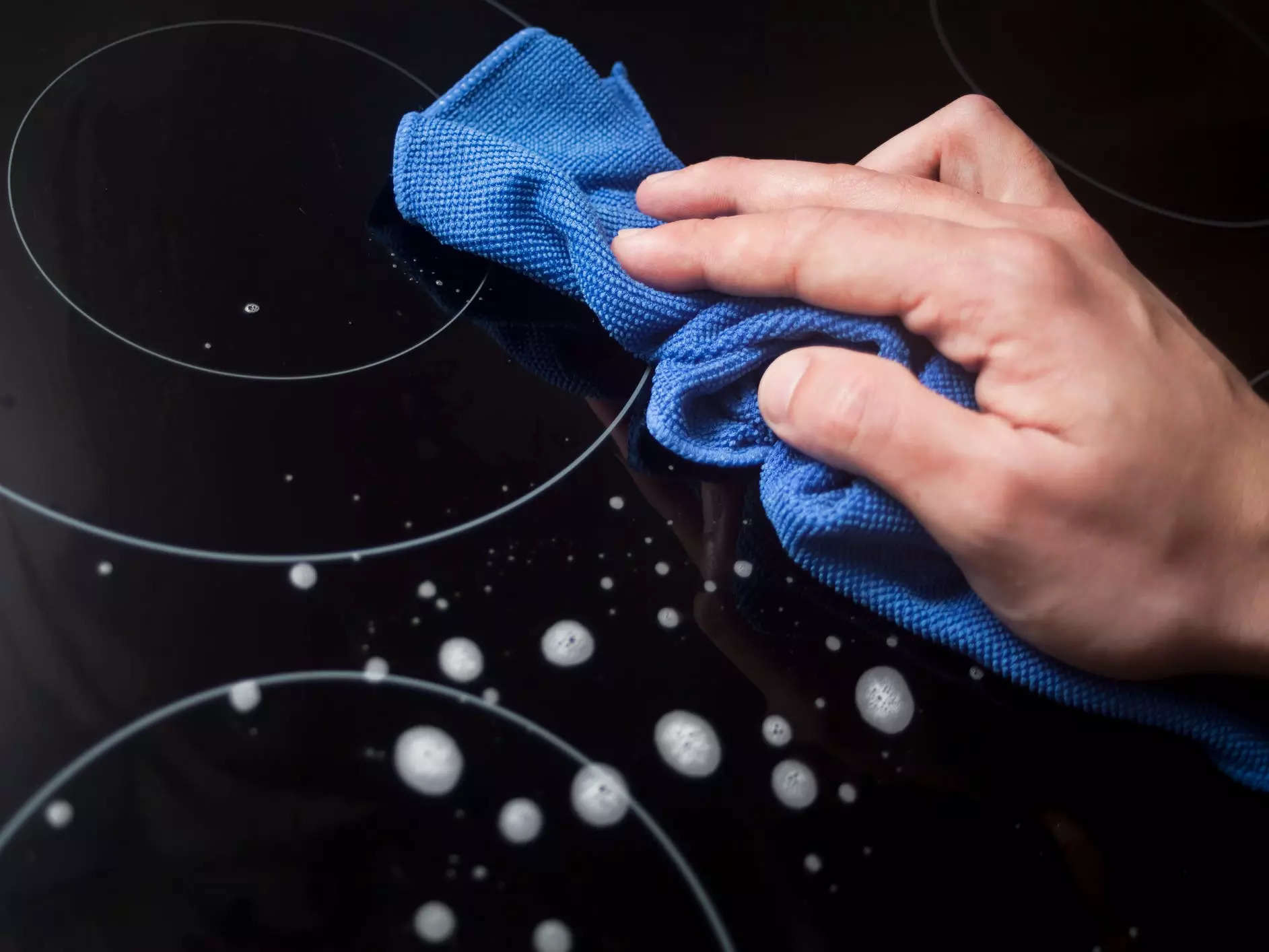 Hand using a microfiber towel on a glass cooktop
