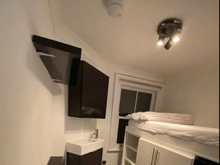 The main space in the tiny apartment space has a single high sleeper bed with a wardrobe and storage beneath it, as well as a sink and cupboard, and a fold-away desk.