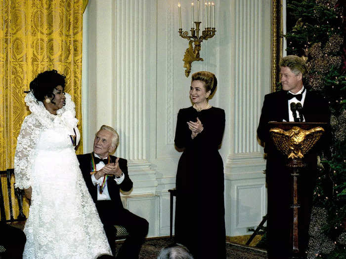 In 1994, Aretha Franklin visited the 42nd president in a wedding-style gown. Her white garment had see-through sleeves, a tall collar, and lace from top to bottom.