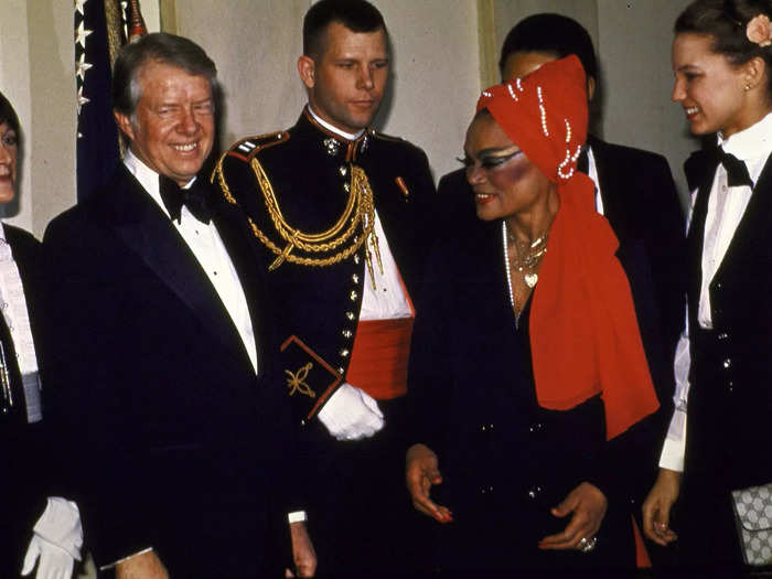 Eight years later, Eartha Kitt wore a suit-style dress and red headscarf to meet Jimmy Carter. She accessorized with layered necklaces, bold blush, and standout eye makeup.