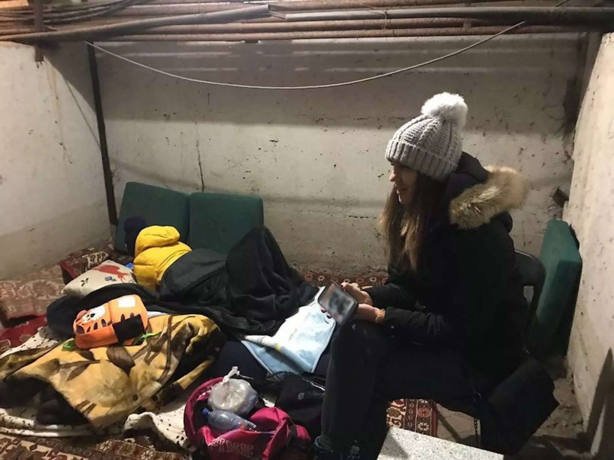 Marina Shut sits in a basement with her coat on with her six-year-old son