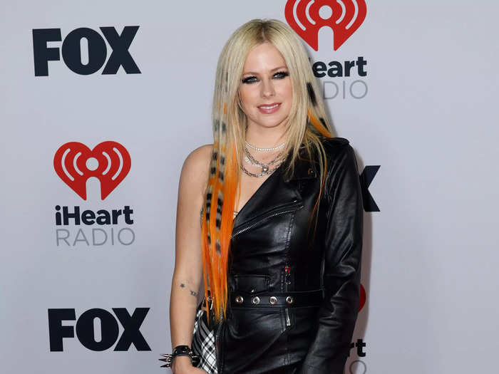 Avril Lavigne honored her rockstar legacy with orange hair and a tartan detail on her asymmetric leather minidress.
