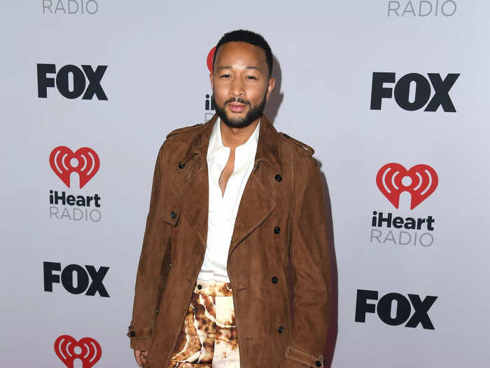 John Legend walked the red carpet in a 70s-style ensemble with statement print pants, cream boots, and a brown trench coat.