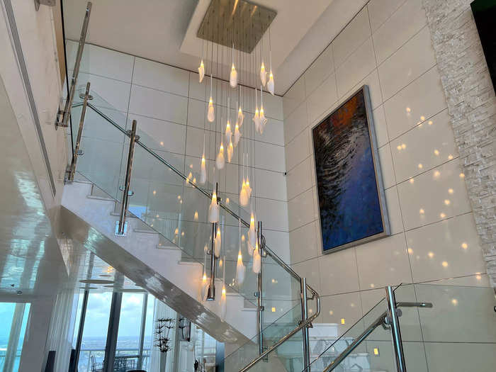 A glass and marble staircase separated the living room from the dining space. The statement light fixture reflected against the wall like a disco ball.