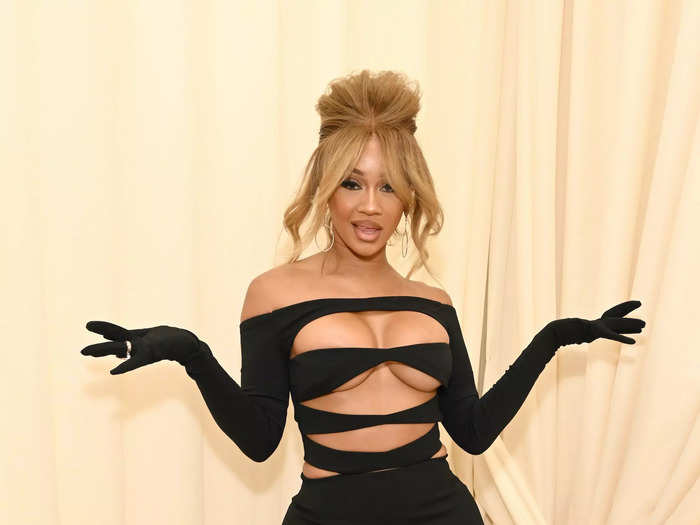 Saweetie chose daring cutouts for the event. Her black, off-the-shoulder dress had attached gloves, four tears across its bodice, and a floor-length skirt.