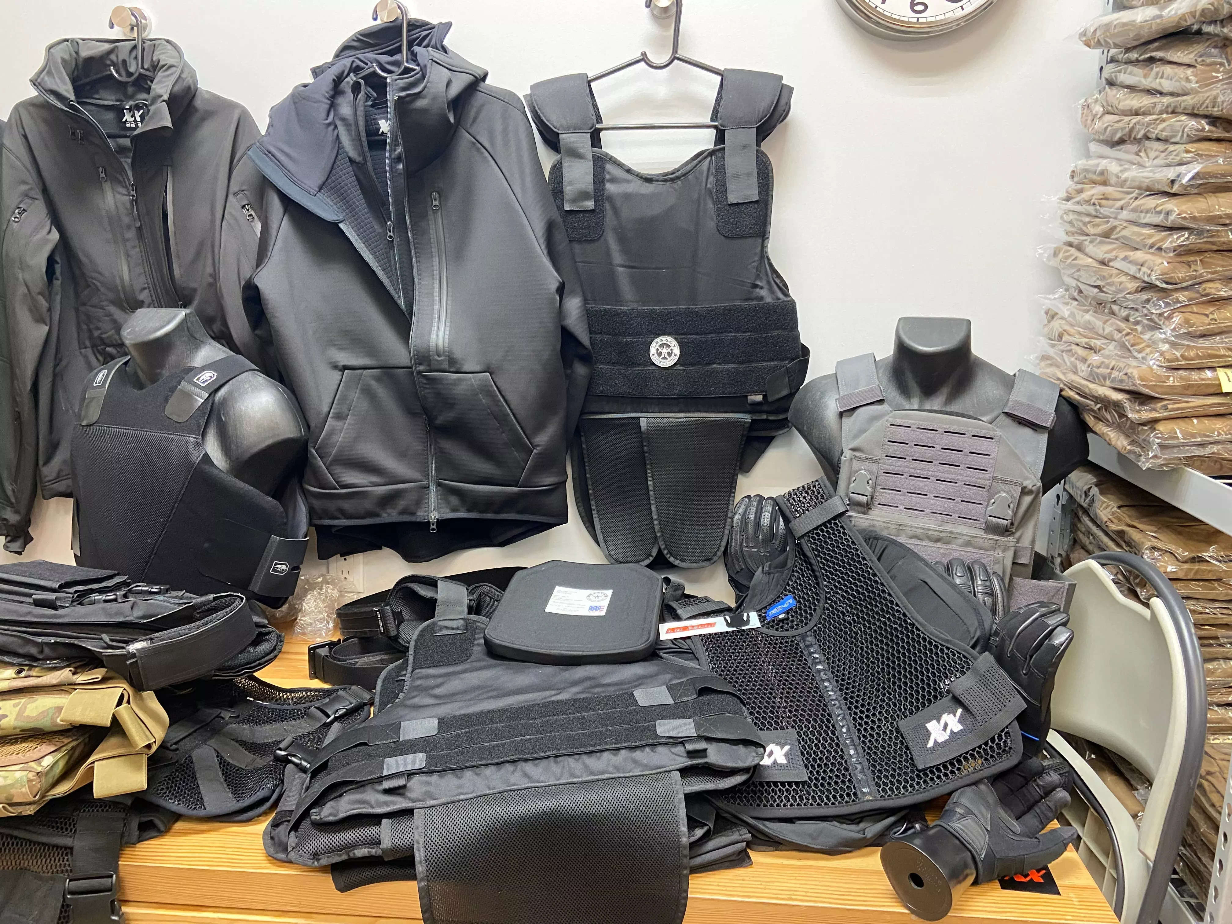 Black vests and other body armor accessories are seen displayed on a table and hanging above.
