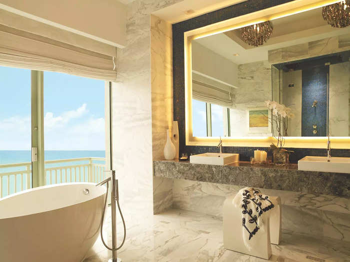 Inside the bathroom, a soaking tub is positioned by floor-to-ceiling windows with an ocean view.
