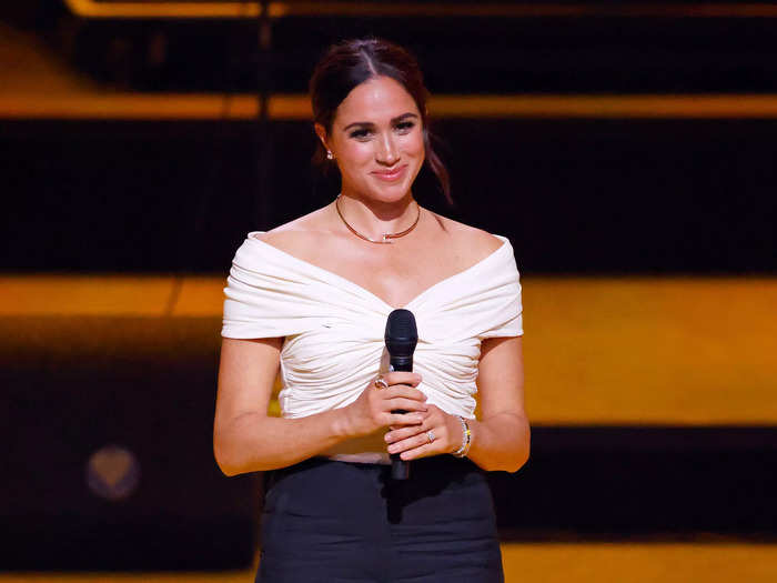 Markle introduced Prince Harry during the opening ceremony in a smart yet daring cream-and-navy outfit and a simple Cartier necklace.