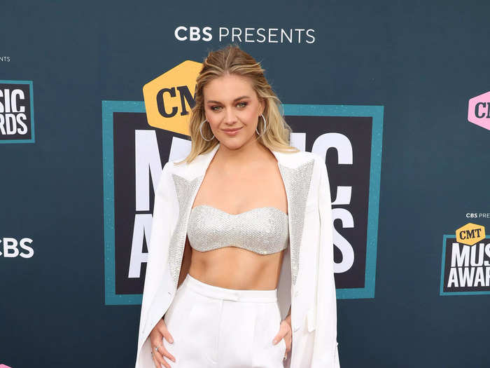 Kelsea Ballerini wore a white suit jacket and tailored pants, along with a sparkling bra, to host the CMT Awards from her house on April 11.