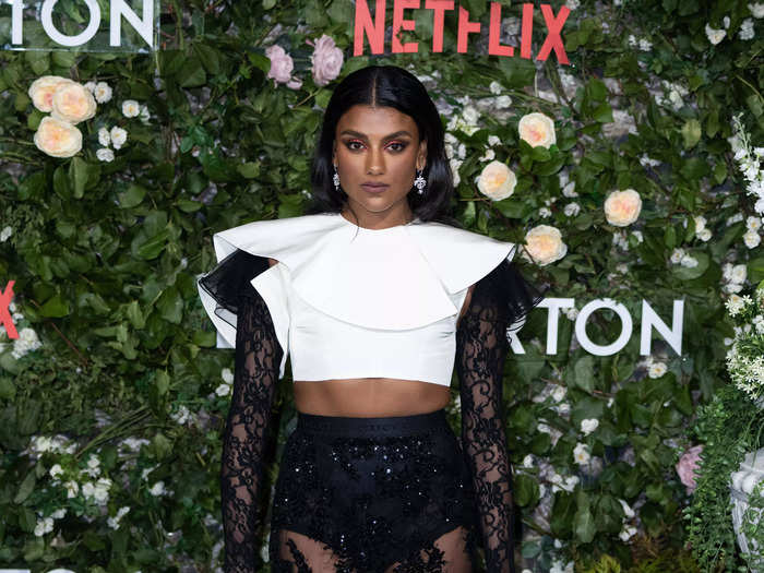 Simone Ashley, the latest star of "Bridgerton," attended its premiere on March 22 wearing a structured white crop top with lace sleeves and a black lace skirt with an olive-green hem.