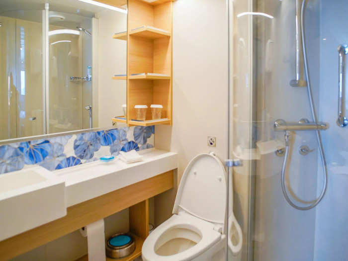 Next to the couch and desk area, a small bathroom utilized clever storage hacks like placing the trash can and toilet paper under the counter.