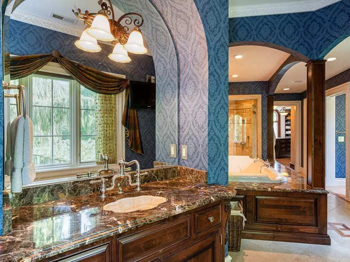 There are eight bathrooms in the house, including the master bathroom, which is covered in patterned blue wallpaper.