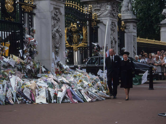 In an iconic yet somber photograph, Queen Elizabeth and Prince Philip can be seen walking past a public memorial to Princess Diana at the gates of Buckingham Palace.