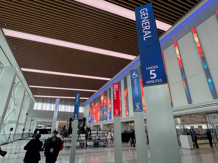 Tall digital boards stand just before the checkpoint, displaying TSA wait times for general security, Sky Priority, people with disabilities, Clear, TSA PreCheck, and family assist.