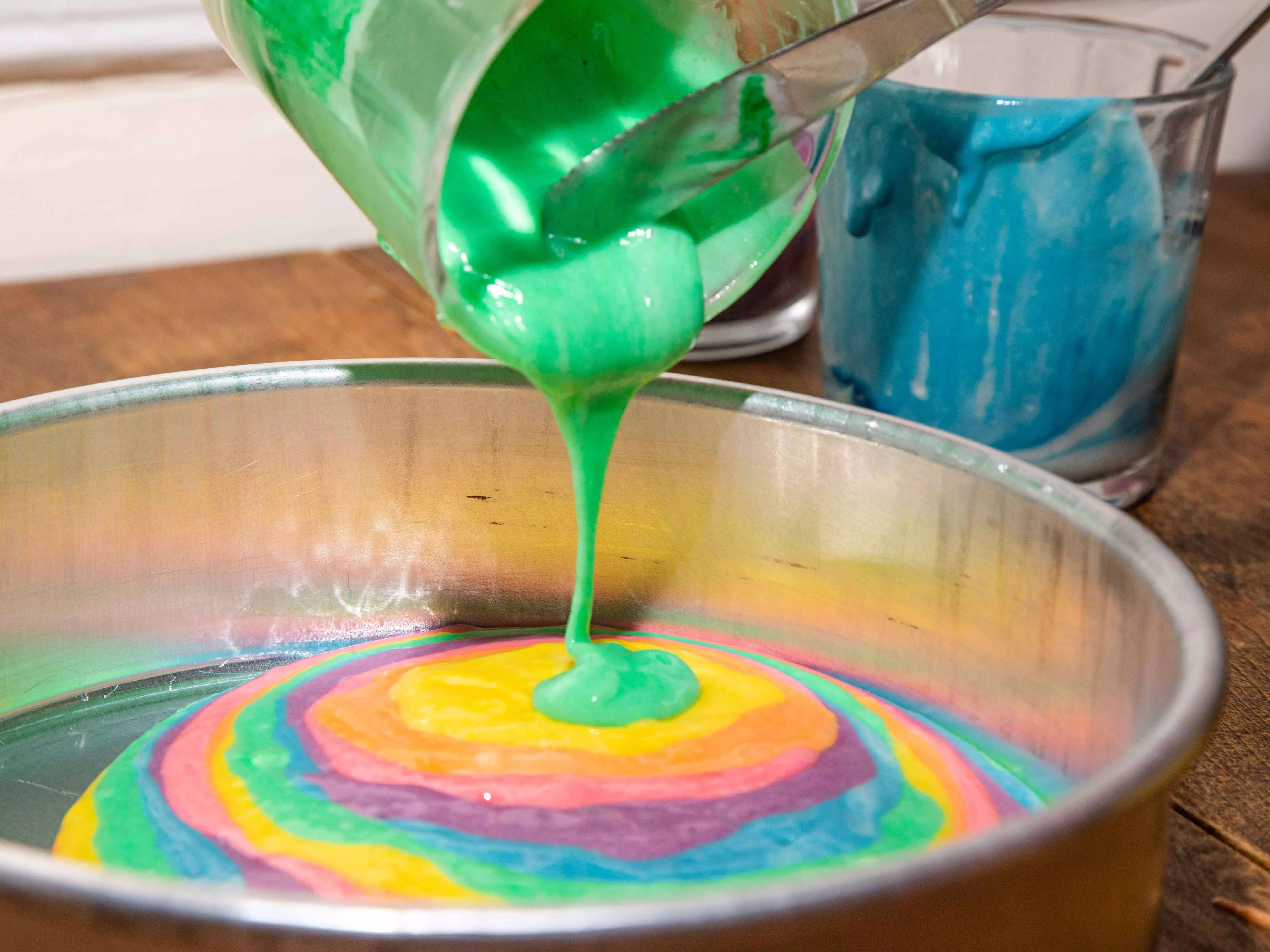 cake batter being poured into a pan to make tie dye rainbow cake