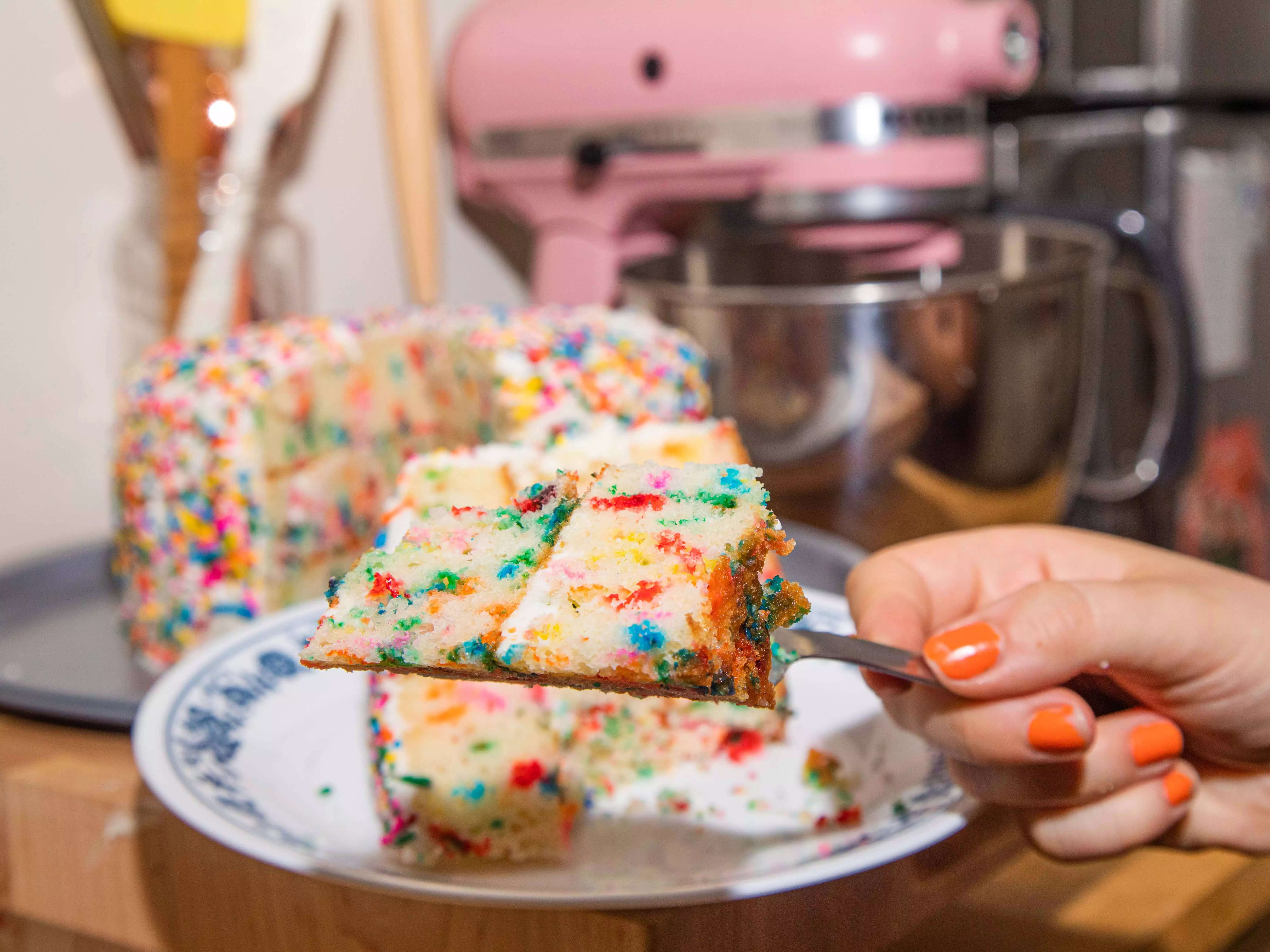 A hand holding up a bite of rainbow funfetti cake