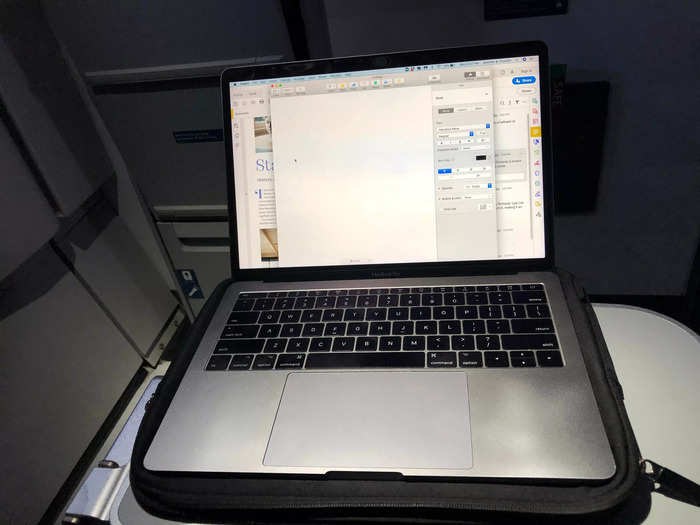 My economy seat had a bi-fold tray that opened from my armrest. When fully open, it was large enough to accommodate my 13-inch MacBook Pro.
