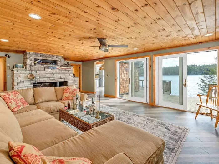 A wood-paneled ceiling spans the entire length of the living room. Large sliding glass doors lead out to the deck, which overlooks the lake.