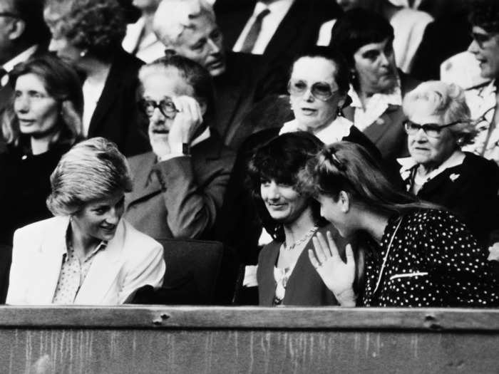 Princess Diana and her sister-in-law Sarah, the Duchess of York, talk over the person seated between them while courtside at Wimbledon in 1988.