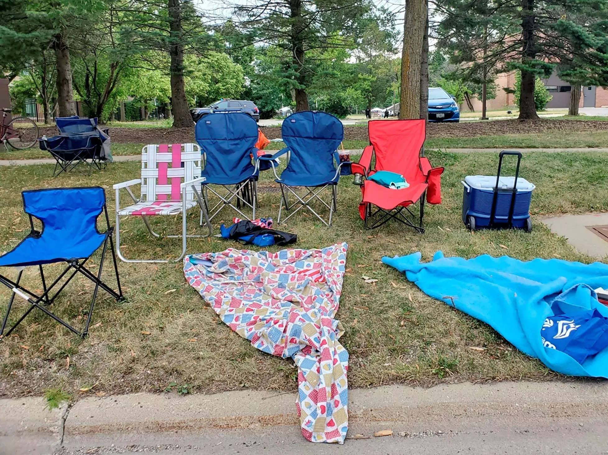 empty lawn chairs and blankets with cooler in grass beside street
