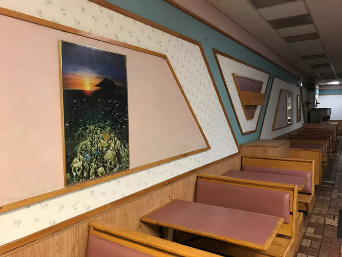 The walls appear to have white paper with a subtle gray pattern, along with pink and blue accents. There are also some framed scenic images throughout the restaurant.