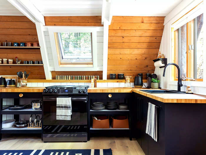 The A-frame cabin spans 792 square feet and features a steeply pitched wood ceiling. The kitchen has a modern design, with wood cabinets and sleek, dark finishes.