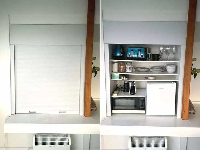 A kitchen cabinet opened up to reveal a small fridge, microwave, coffee maker, kettle, and toaster.